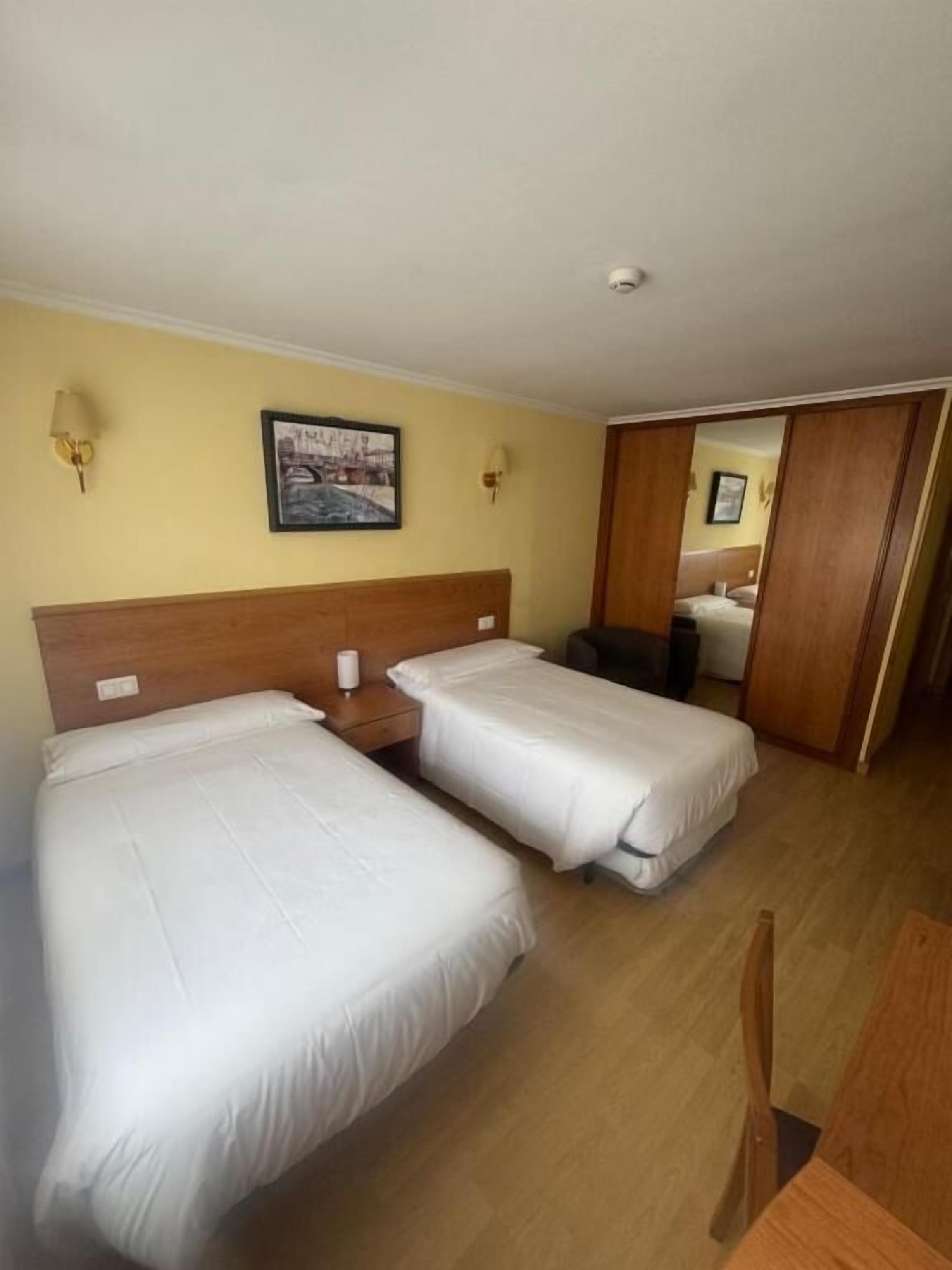 A hotel room with two single beds, a wooden headboard, a wall-mounted picture, and a mirror.