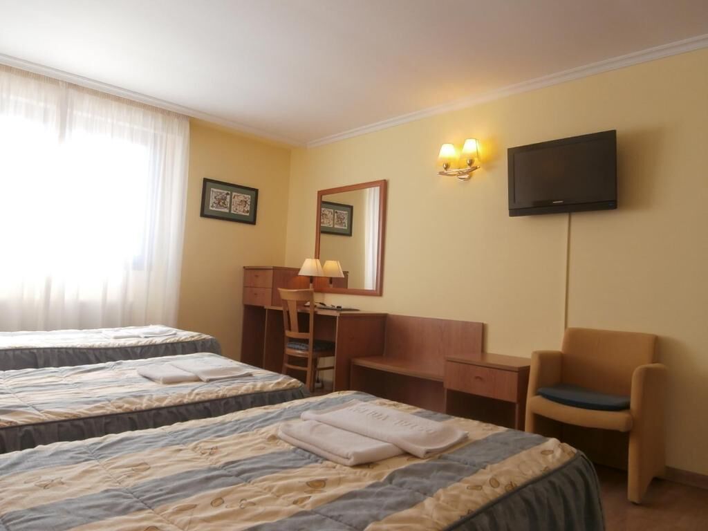 Habitación de hotel con dos camas, un escritorio, una silla, un televisor y una ventana con cortinas.