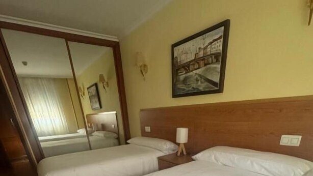 A hotel room with two beds, a wooden headboard, a painting on the wall, and a mirror. - Hostal El Volante (Estella)