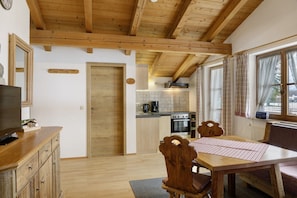 Ein Holzinterieur mit Esstisch, Stühlen, einem Fernseher auf einem Schrank, einer Küchenzeile mit Geräten und einem Fenster mit Vorhängen.