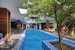 A modern indoor swimming pool with a tiled edge, surrounded by wooden flooring and furniture. - Palette Hotel Seminyak  (Seminyak)