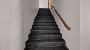 Eine Treppe mit schwarzen Stufen und einem hölzernen Geländer, die zu einer Tür mit der Aufschrift 'EXIT' führt.