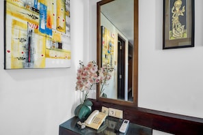 A hotel reception desk with a telephone, a vase with flowers, and a large abstract painting on the wall. - Palette Hotel Seminyak  (Seminyak)