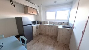 Cocina compacta con armarios de madera, un refrigerador, un microondas y un ventanal que proporciona luz natural.