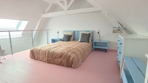 Un dormitorio con una cama litera, un tragaluz, una cama con edredón color crema y un aparador azul.