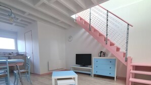 Una habitación con piso de madera, una escalera rosa, una mesa azul y un televisor.