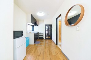 A narrow hallway with a kitchen area on the left, a wooden floor, and a mirror on the right wall. - Kita-Shinjuku Inn House, 3LDK 70m2 Detached House in Shinjuku Area (新宿区)