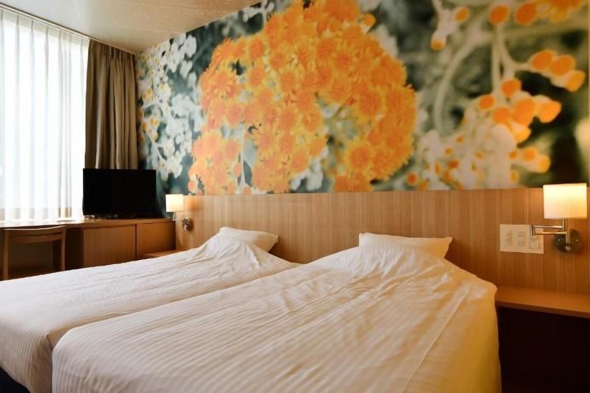 Quarto de hotel com duas camas, televisão, escrivaninha e um mural floral na parede.