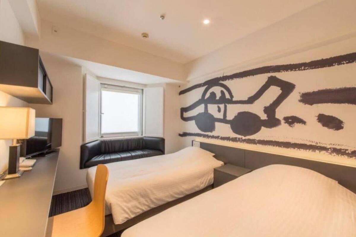Ein Hotelzimmer mit zwei Betten, einem Schreibtisch, einem Stuhl, einem Fenster und einem Wandbild.