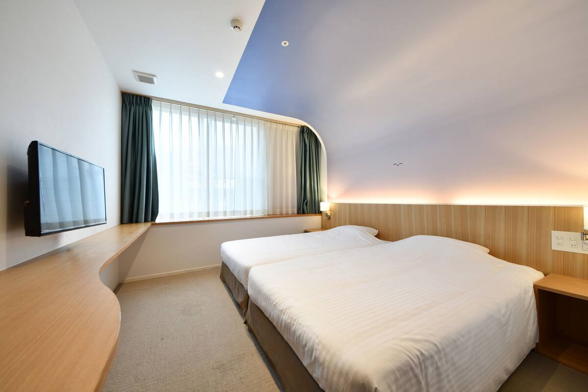 Ein Hotelzimmer mit Bett, Fernseher, Fenster mit Vorhängen und einem Holzkopfteil.