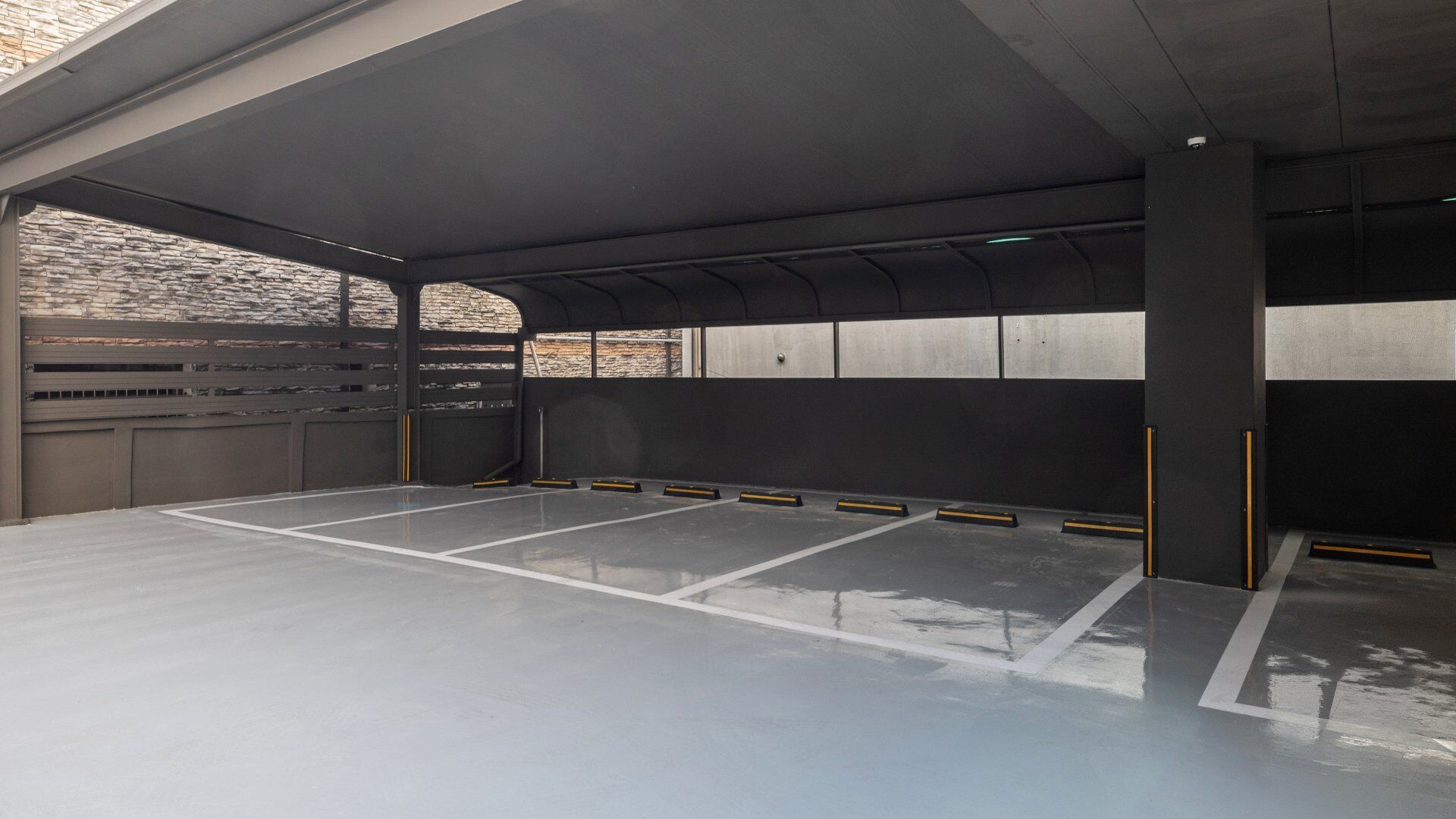 A parking garage with multiple parking spaces, concrete walls, and a stone wall in the background.