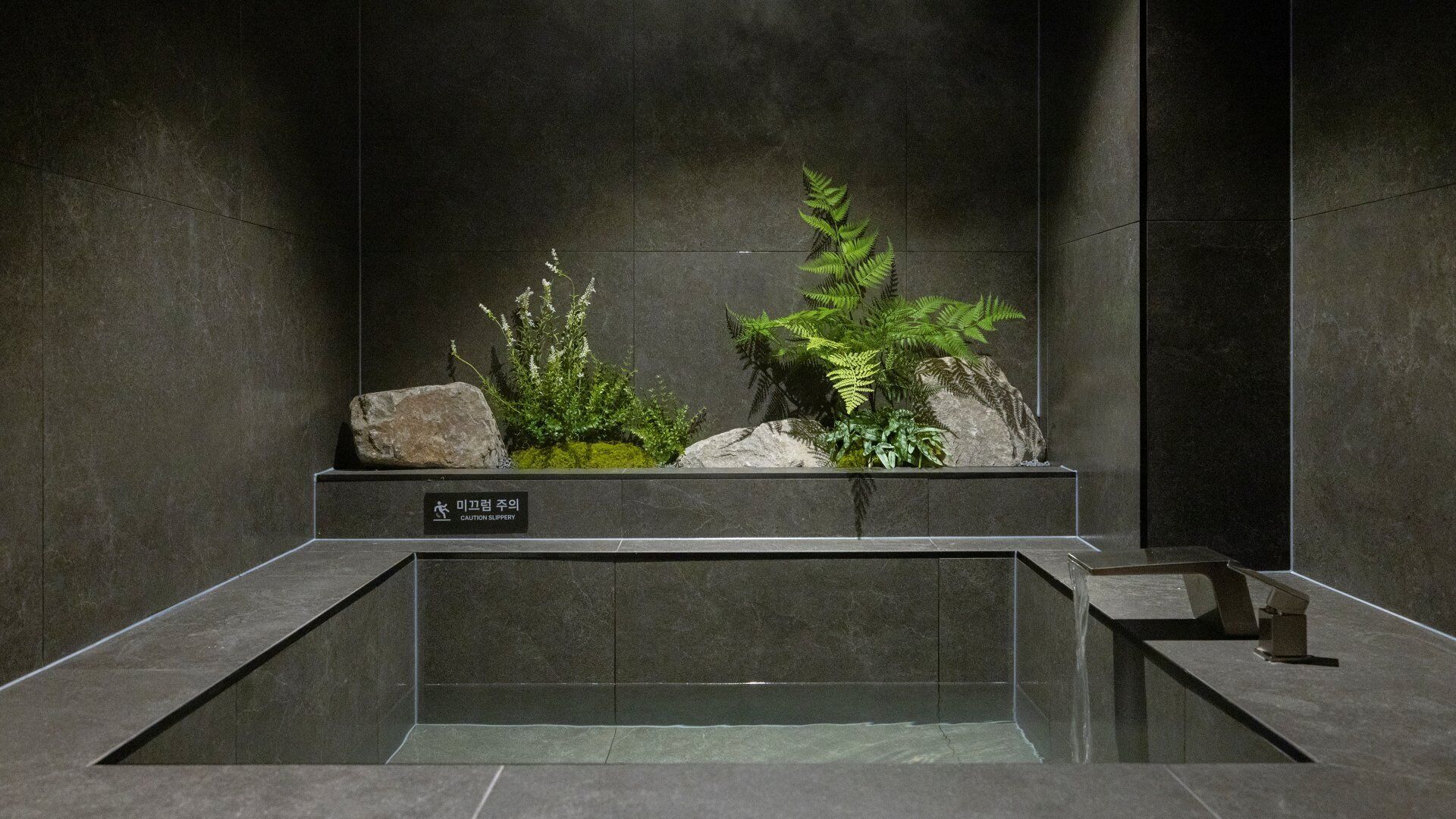 Une salle de bain avec un lavabo en pierre, un panneau d’avertissement et une petite cascade décorative.