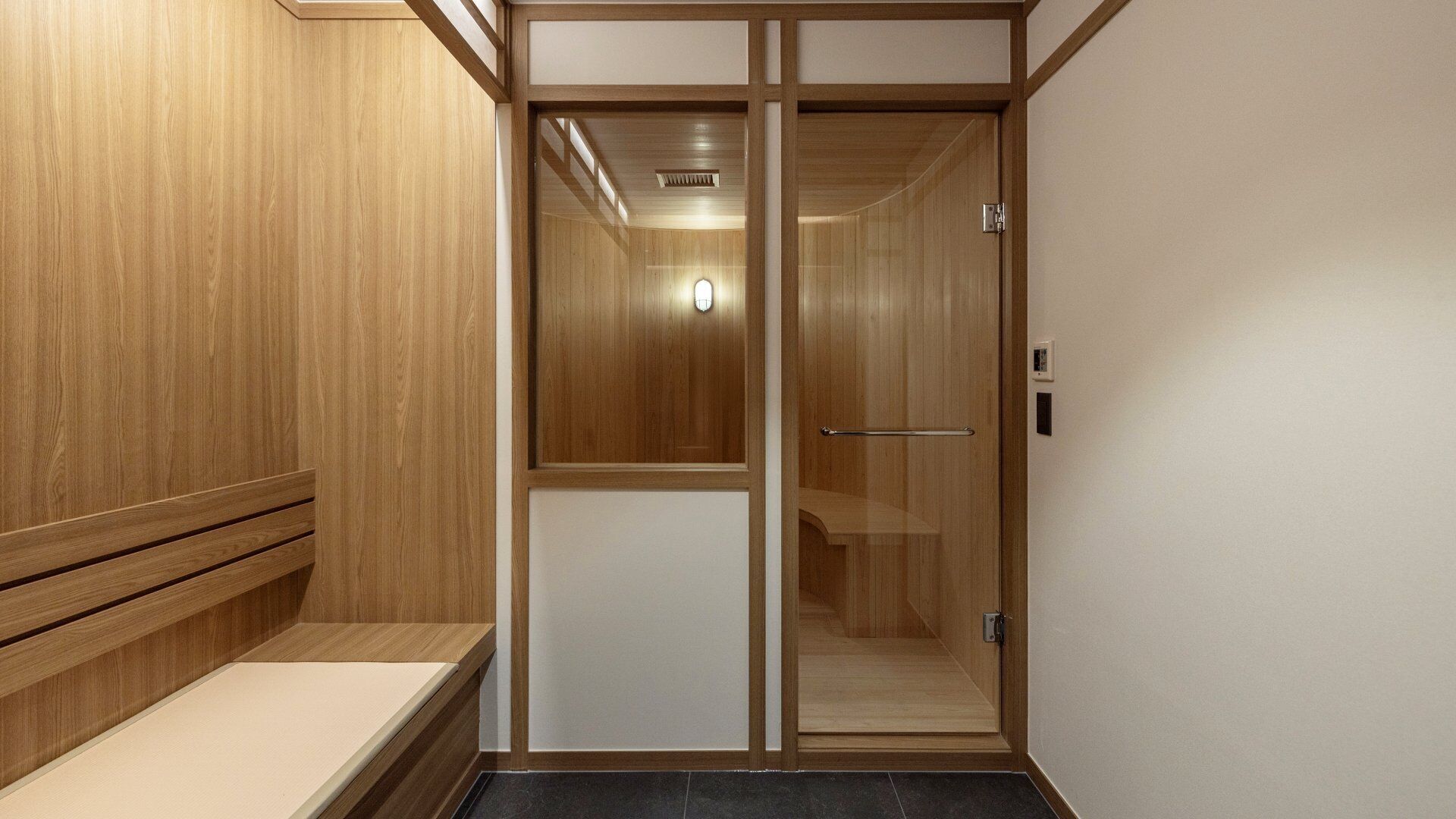 A wooden interior with a bench, a sliding door, and a light fixture.