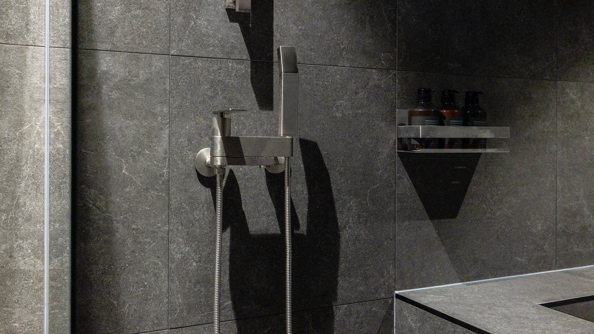 A modern bathroom with a shower, a towel rack, and a soap dispenser.