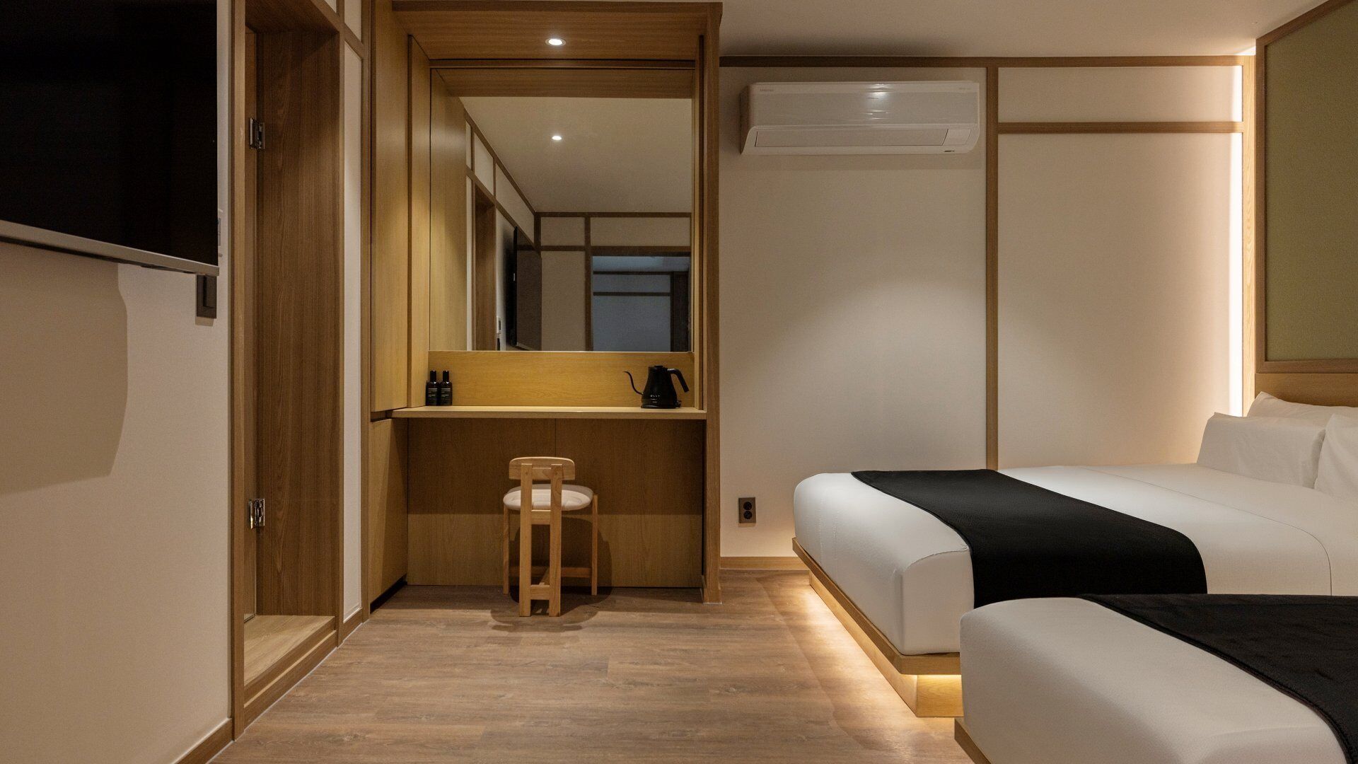 Una habitación de hotel con cama, escritorio, silla, aire acondicionado y espejo.