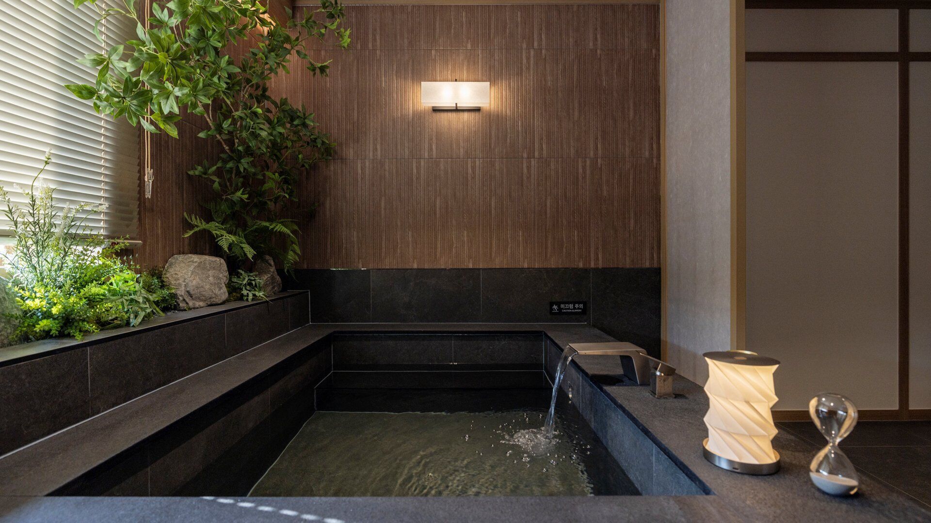 A modern bathroom with a wooden wall, a black bathtub, and a small sink.