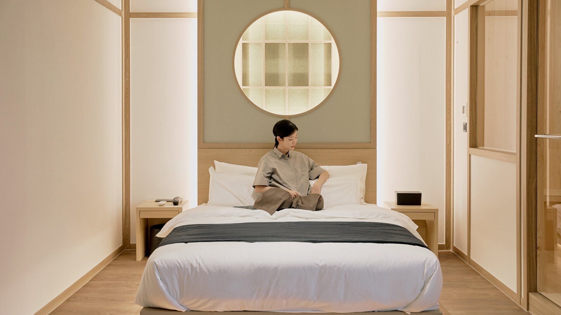 A hotel room with a bed, a nightstand, a round window, and a wardrobe.