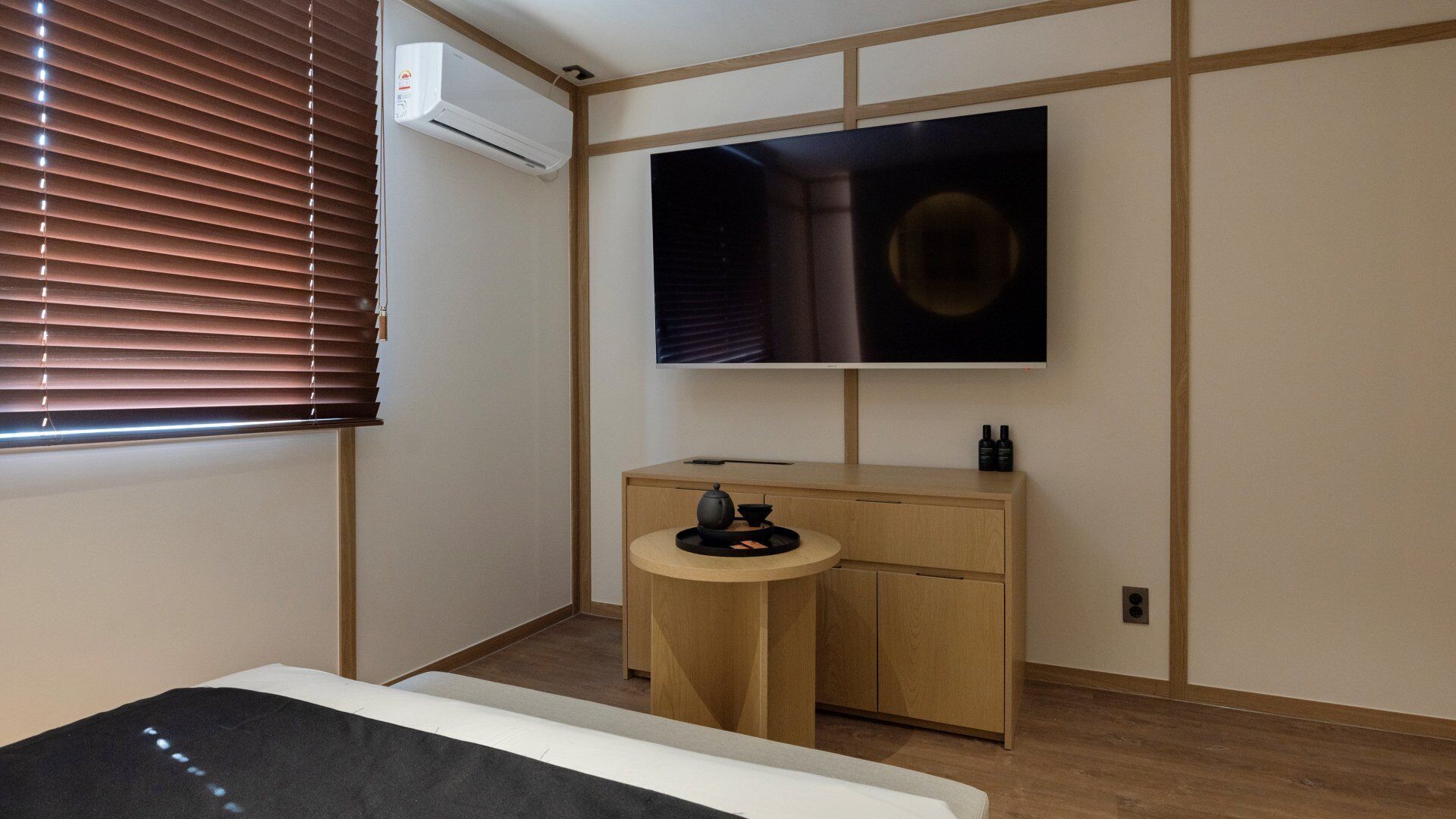 A bedroom with a bed, a TV, a desk with a chair, and an air conditioner.
