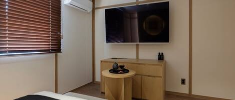 A bedroom with a bed, a TV, a desk with a chair, and an air conditioner.