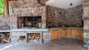 A stone fireplace with a built-in grill, wooden cabinets, and a stone wall. - Apartman Bonaca by Villas Guide (Kuceli)