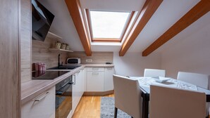 A compact kitchen with a skylight, wooden beams, white cabinetry, and a dining area with a table and chairs. - Apartman Bonaca by Villas Guide (Kuceli)