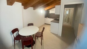 A dining area with a round table and four chairs, a kitchen with white cabinets, and a shower area. - Charming Apartment for 4 Guests – Relax and Comfort near Venice (Venezia)