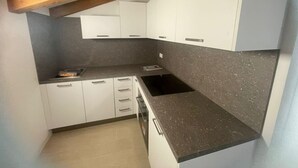 A compact kitchen with white cabinets, a black countertop, and a wooden ceiling beam. - Charming Apartment for 4 Guests – Relax and Comfort near Venice (Venezia)