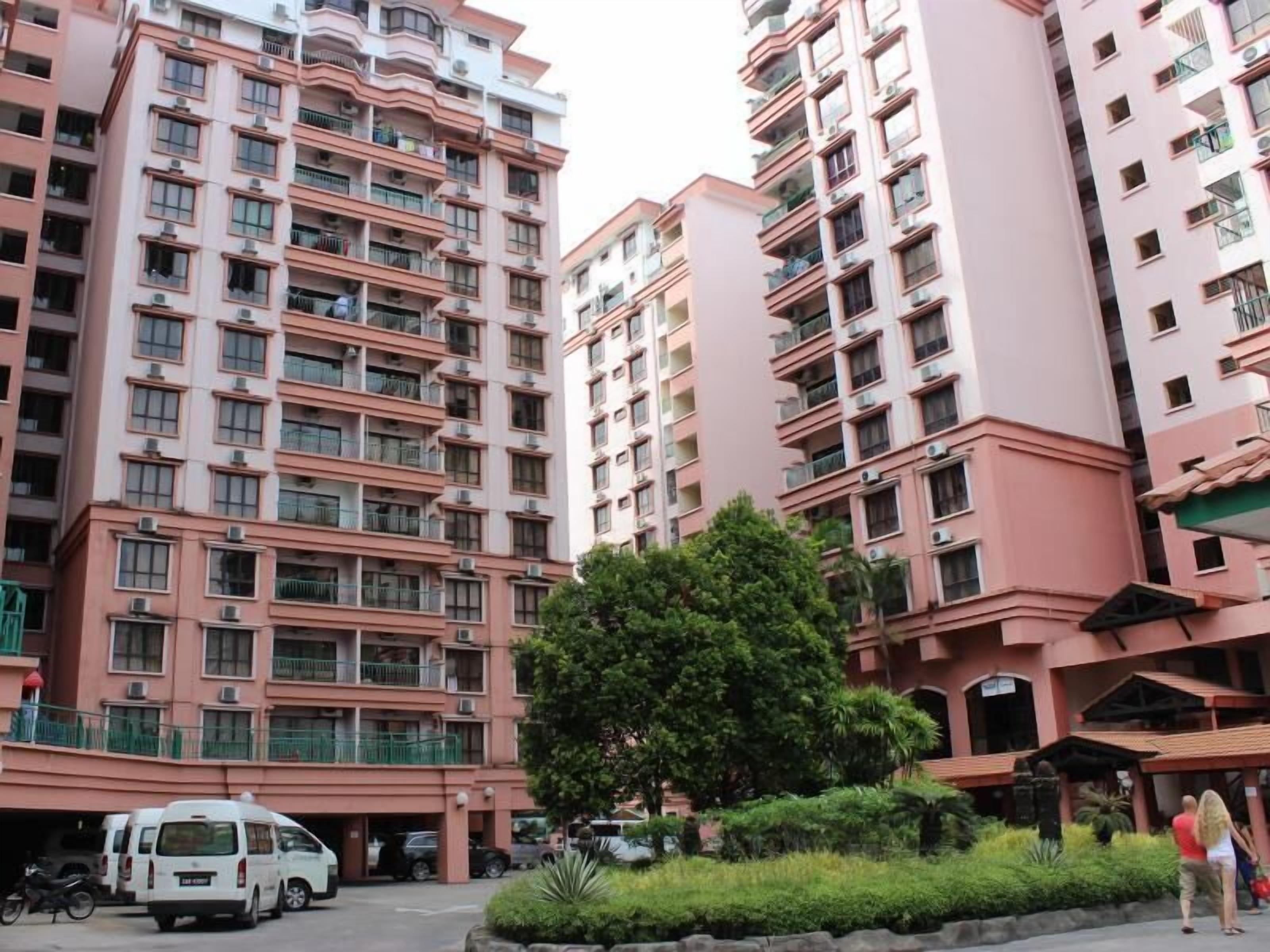 A multi-story residential building with balconies, a parking area, and a small garden.