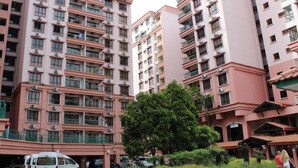 Um edifício residencial com vários andares, varandas, área de estacionamento e um pequeno jardim.