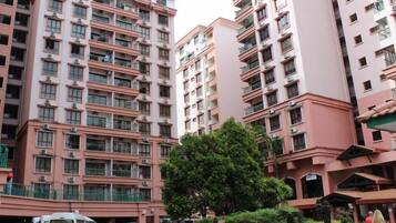 A multi-story residential building with balconies, a parking area, and a small garden.