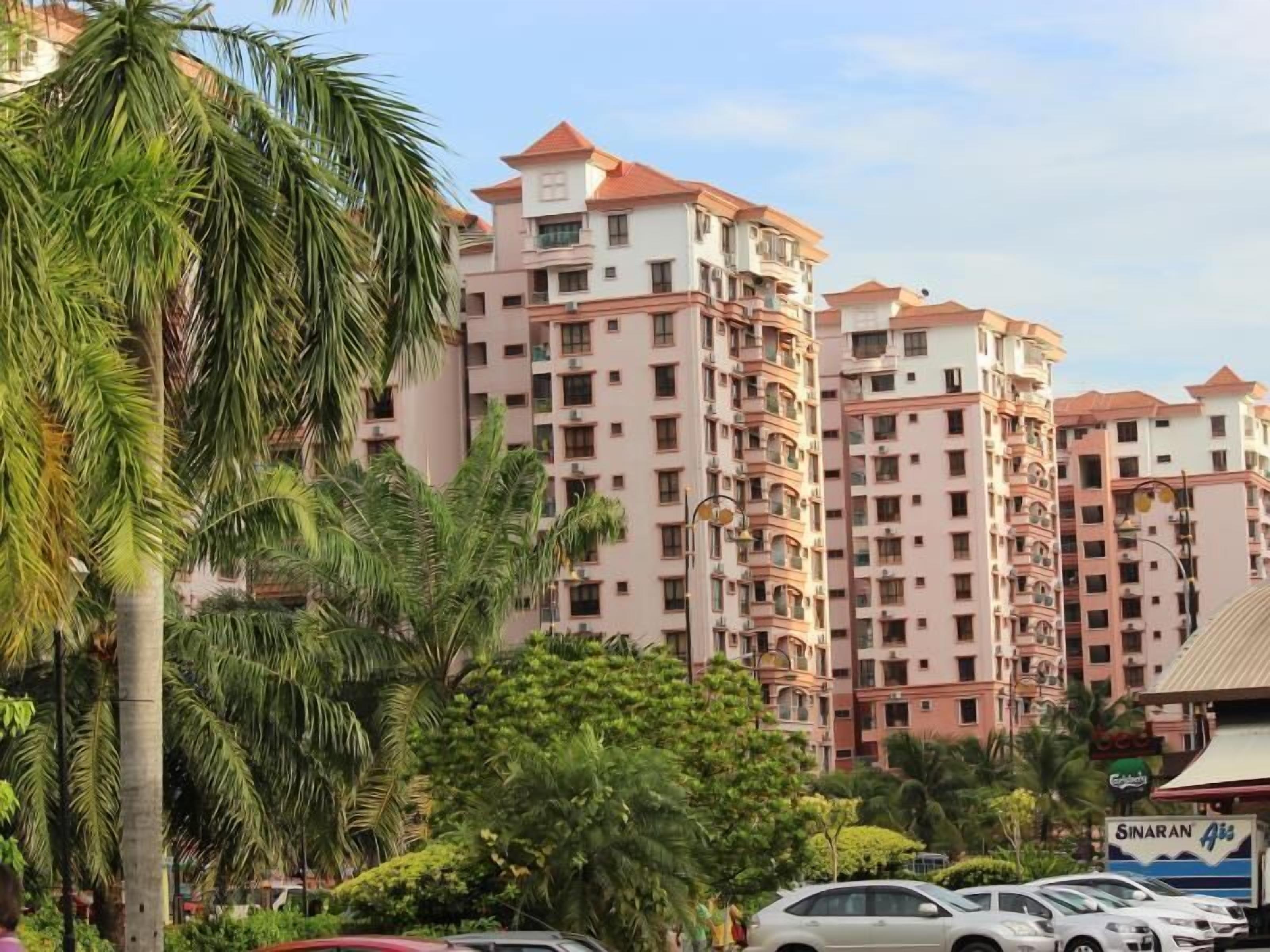 A multi-story residential building with balconies, surrounded by greenery and parked cars.