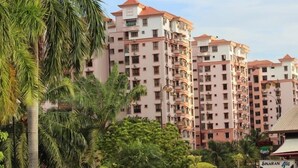 Edifício residencial com vários andares e varandas, cercado por vegetação e carros estacionados.