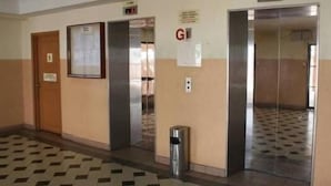 Corredor com dois elevadores, um cesto de lixo e uma porta com sinalização.