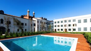A swimming pool with a wooden deck, surrounded by a courtyard with buildings and greenery. - Spacious Apartment for 6 Guests – Elevator Access near Venice (Venezia)