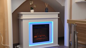 A modern fireplace with a blue light, a white mantel, and a small vase with flowers.