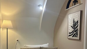 A bedroom with a bed, a lamp, a wall-mounted artwork, and a ceiling light.