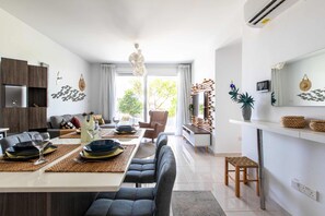 A modern kitchen with a dining area, featuring a central island, built-in wooden cabinets, and a large window providing natural light.