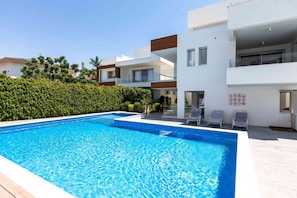 Un edificio residencial moderno con piscina, mobiliario exterior y un jardín bien cuidado.