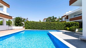 A swimming pool with a clear blue water surface, surrounded by modern buildings and a well-maintained hedge. - Lemon Tree 1-BR Apt & Pool in Livadia (Larnaca)