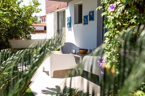 Un espace extérieur moderne avec des sièges, comprenant une table et des chaises blanches, une petite fenêtre et des décorations murales en forme d’étoiles de mer.