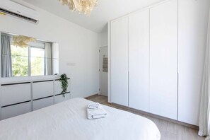 Un dormitorio con una cama grande, un armario, una ventana con cortinas y una planta.