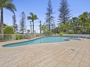A swimming pool with a tiled deck, surrounded by palm trees and other vegetation. - Bright 2 Bed Apartment With Ocean Views (Gold Coast)