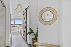 Um corredor com vista para o exterior, um espelho de vime e uma planta.