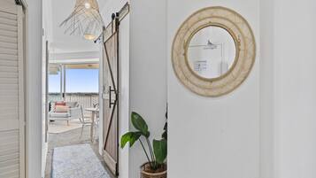 A hallway with a view to an outdoor seating area, a wicker mirror, and a potted plant.