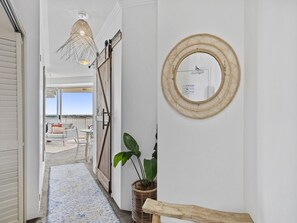 A hallway with a view to an outdoor seating area, a wicker mirror, and a potted plant. - Bright 2 Bed Apartment With Ocean Views (Gold Coast)