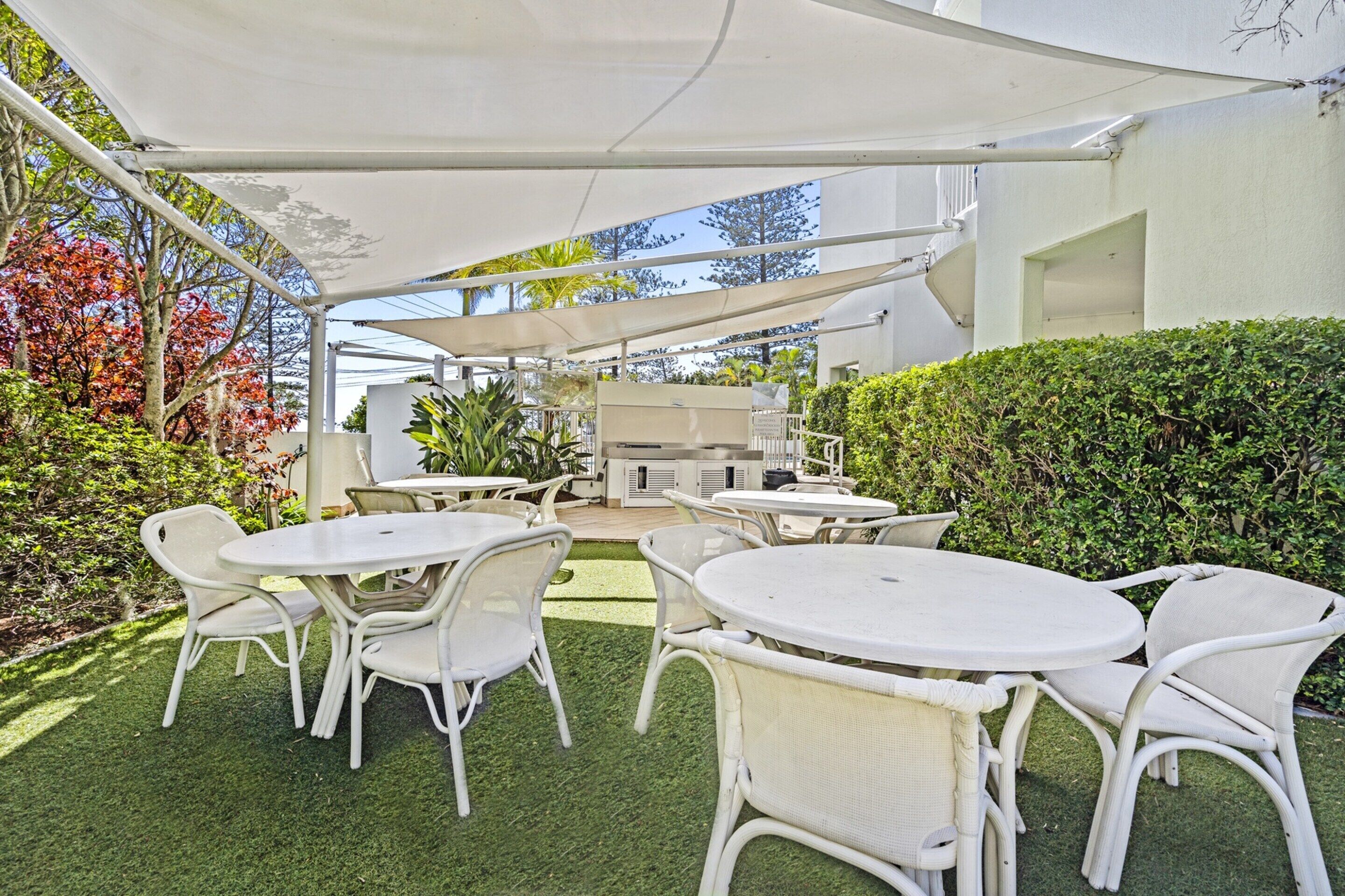 An outdoor patio area with white tables and chairs, a barbecue grill, and a white canopy.