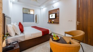 Habitació d'hotel amb un llit, escriptori amb un plat de fruita, una cadira, una porta de fusta i un ventilador de sostre.