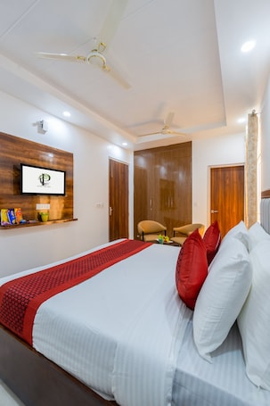 A hotel room with a bed, a TV mounted on the wall, a ceiling fan, and a wooden wardrobe.