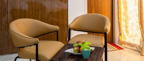 Una habitación con un armario de madera, una puerta de madera, una mesa con frutero y una silla.