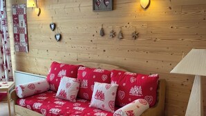 A wooden sofa with heart-patterned cushions, a small wooden stool, and wall-mounted decorative items. - Les 2 alpes, at the foot of the slopes - apartments (Les Deux Alpes)